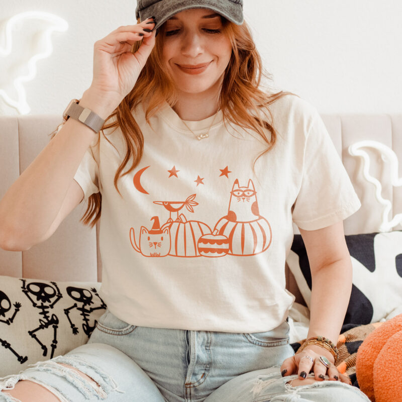 a woman wearing a pumpkin patch cats t-shirt in ivory