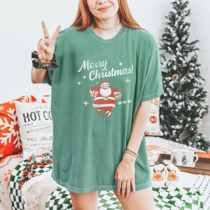 a woman wearing a Show your holiday spirit with the Retro Santa Christmas T-Shirt. This fun Comfort Colors Christmas shirt is garment dyed for a vintage, lived in look from the get go. Soft, heavyweight fabric, short sleeves, and a relaxed, crowd pleasing fit for both men and women. in light green
