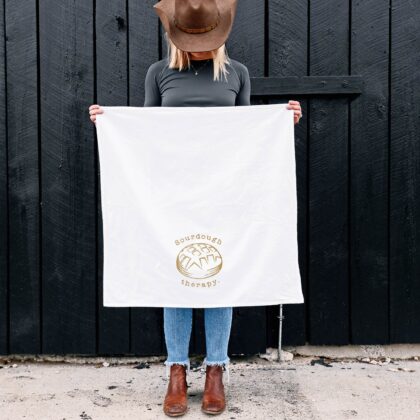 a woman holding up, out in front of herself, an unfolded sourdough therapy tea towel in white