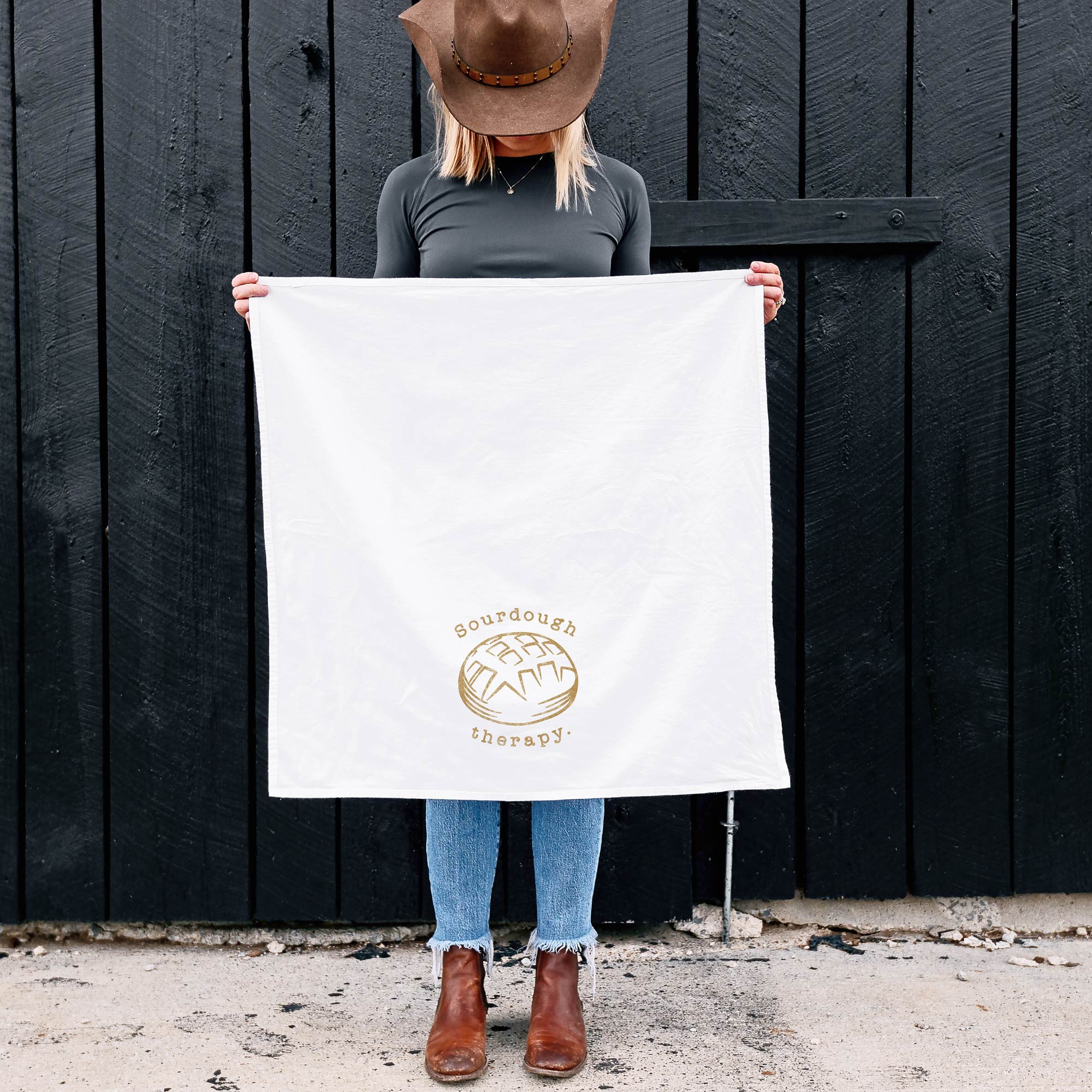 a woman holding up, out in front of herself, an unfolded sourdough therapy tea towel in white
