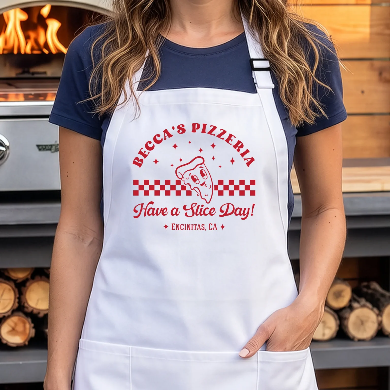 White personalized Retro Pizza apron with red lettering, worn beside an outdoor pizza oven
