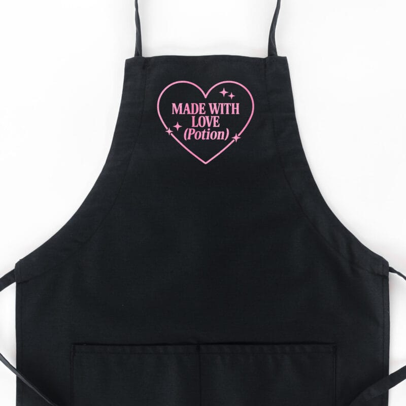 a Made With Love Potion Butcher Apron in black with a flamingo glitter print