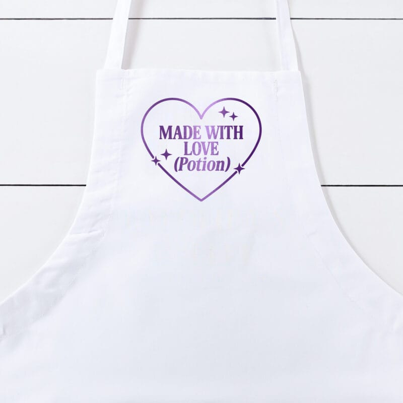 a Made With Love Potion Butcher Apron in white with a purple metallic print