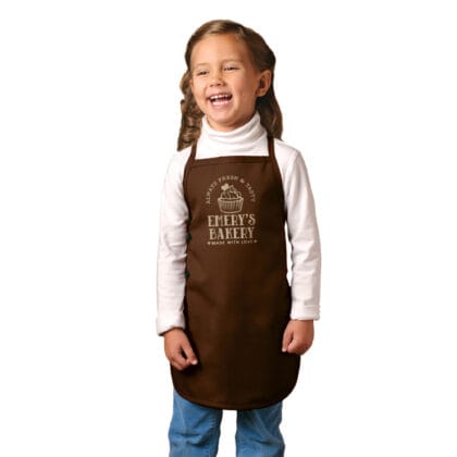 a little girl wearing a premium personalized kids cupcake apron in brown