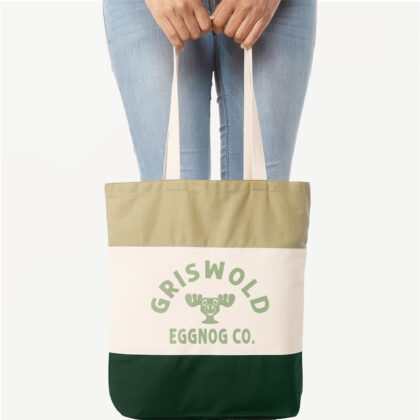 a woman holding a Griswold Eggnog Co. Tote bag in Forest green