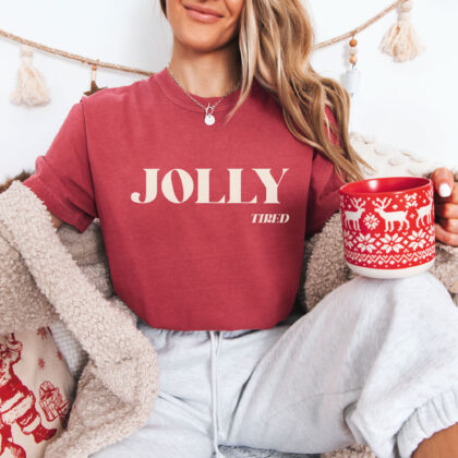 a young woman relaxing in a christmas scene, wearing a Jolly Tired T-Shirt in crimson