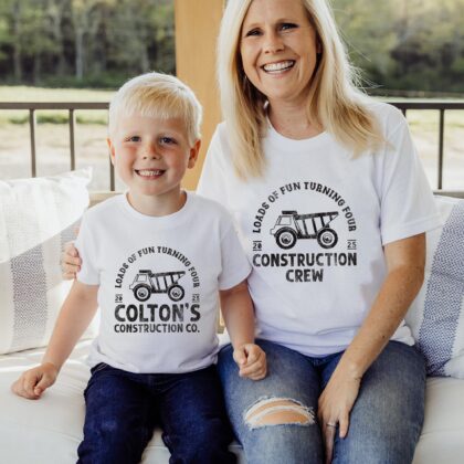 a little boy and woman sitting together on a porch, wearing matching dump truck birthday tees in white. The boy is wearing a personalized birthday construction shirt, the woman is wearing a woman wearing a Construction Crew Shirt