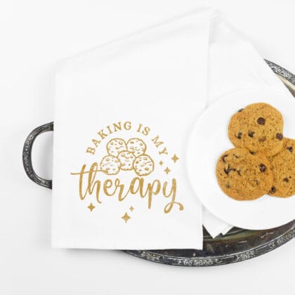 a Cookie Baking Therapy Tea Towel in white that reads "baking is my therapy", displayed next to a plate of chocolate chip cookies