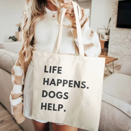 a woman holding a life happens dogs help tote in natural