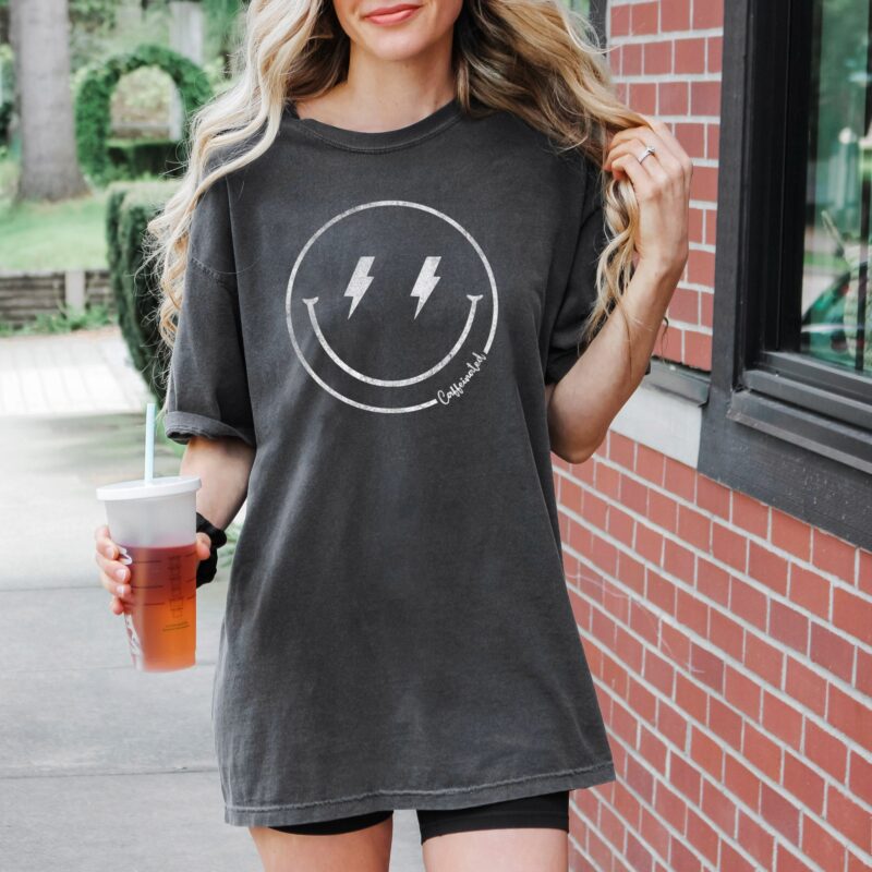 a pretty woman holding a beverage, wearing a retro caffeinated comfort colors tee in pepper