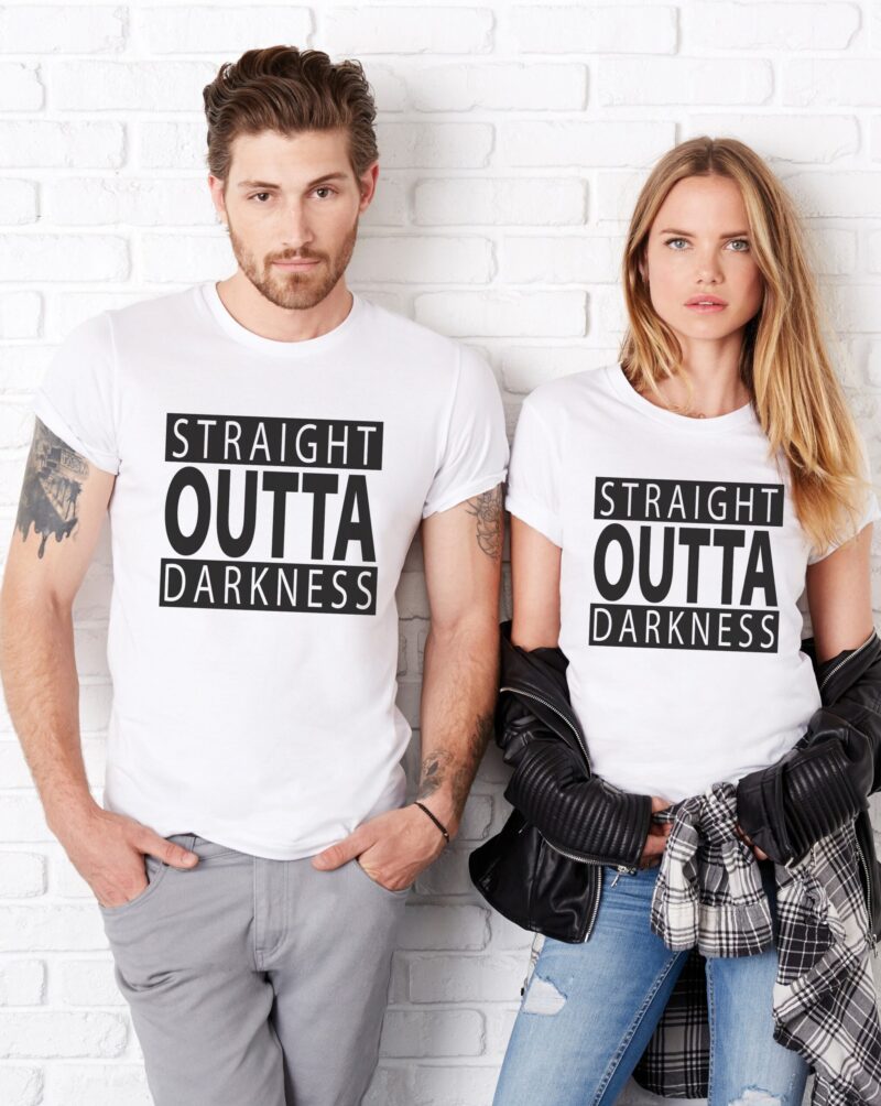 a beautiful young woman and handsome man lean against a wall, wearing straight outta darkness t-shirts