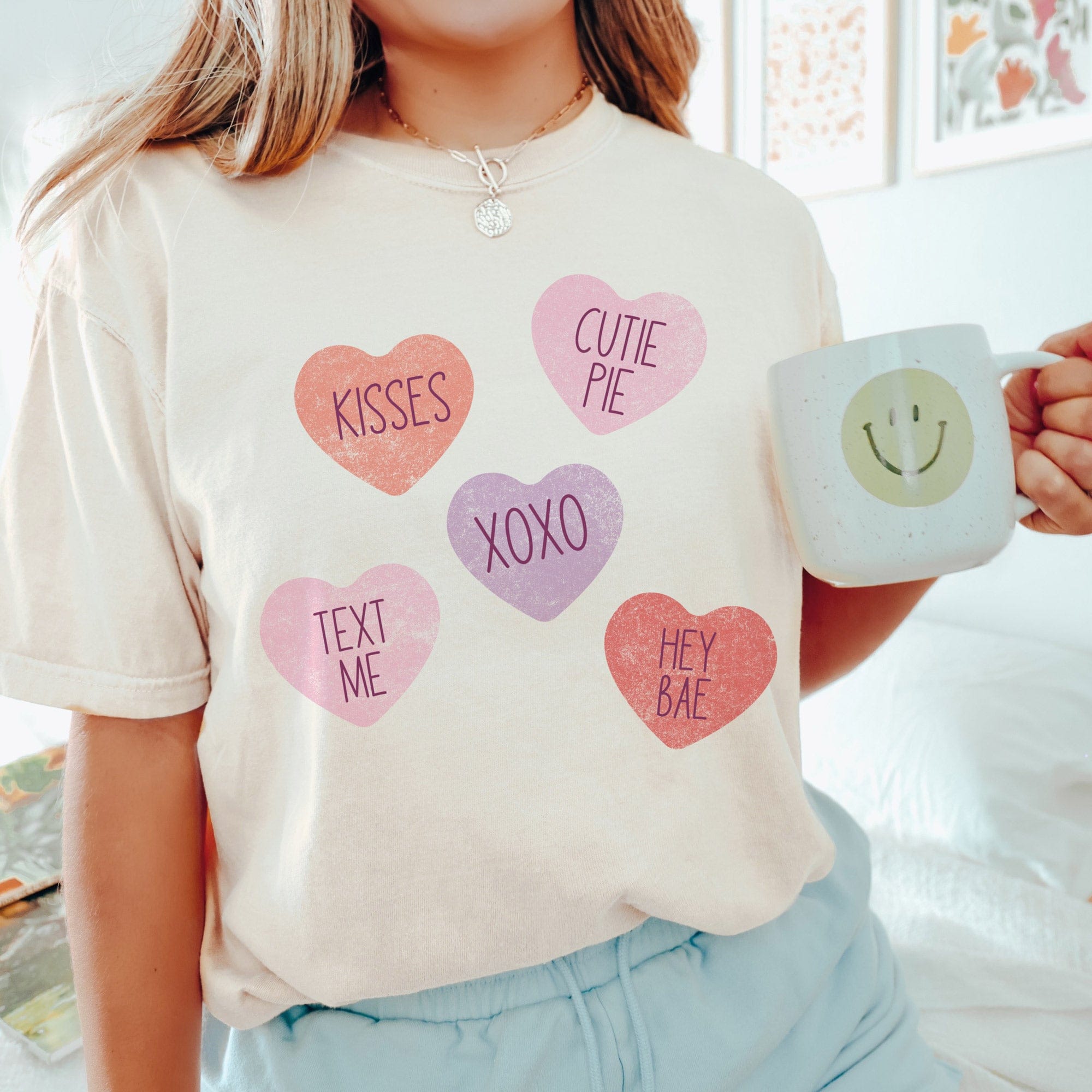 a young woman in a bedroom, wearing a Sweethearts Comfort Colors Tee in ivory